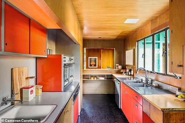 The kitchen has a small cooking island, stainless steel appliances, orange painted shelves and a black floor