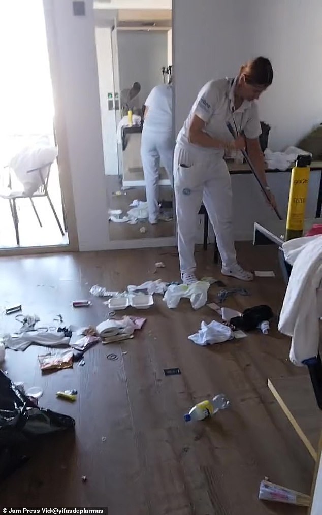 Toilet paper and empty plastic bottles are strewn around the apartment as a housekeeper cleans