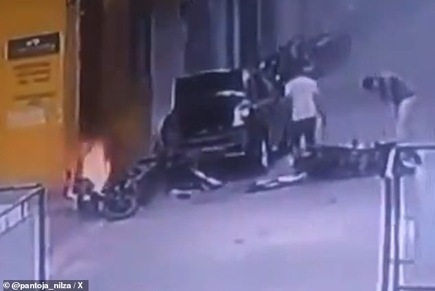 Two teenagers stand by their wrecked motorcycle that fell to the ground after a motorcycle bombing (pictured left in flames). The teenagers were taken to a local medical facility, where they were treated. The extent of their injuries is unknown