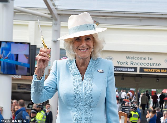 Pictured: Queen Camilla smiles as she prepares to cut a ceremonial ribbon to open a new grandstand at York Racecourse