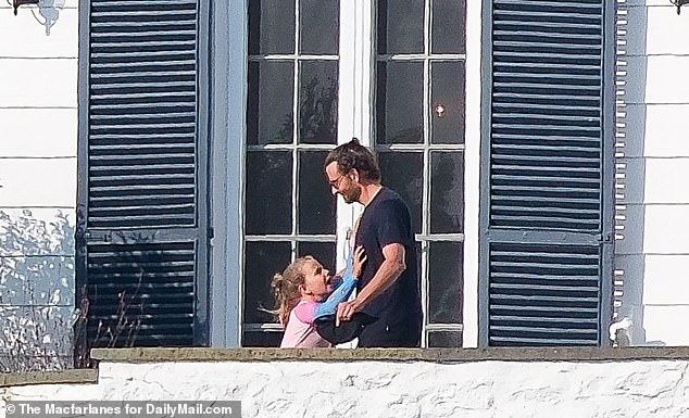 In exclusive photos obtained by DailyMail.com, Bradley enjoys the summer sun with his seven-year-old daughter as they stand on a balcony - and at one point he flashed a big smile during a lighthearted moment