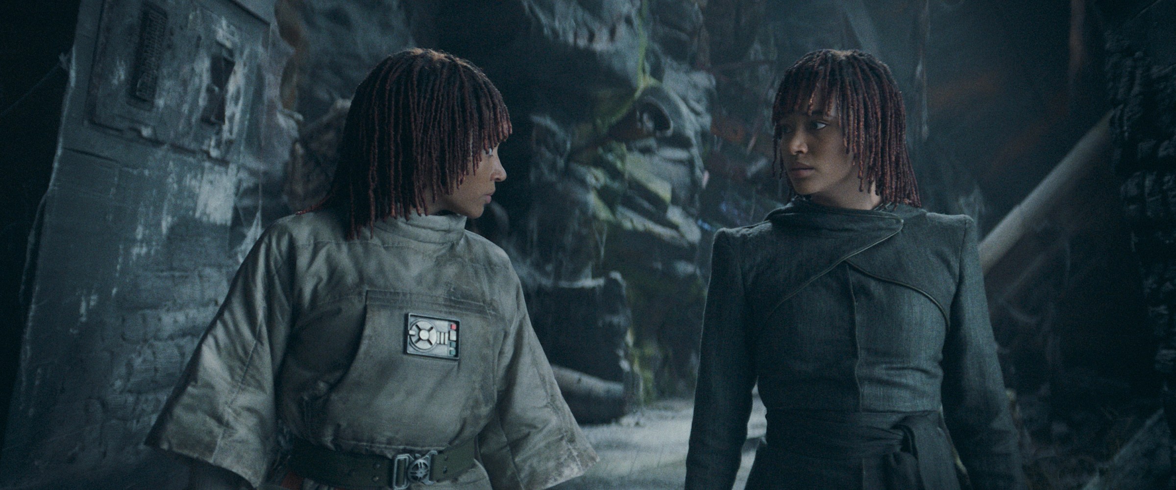 Twin sisters Mae and Osha (both played by Amandla Stenberg) stand in a rough-hewn rock passageway filled with rubble and stare at each other in the Star Wars TV series The Acolyte