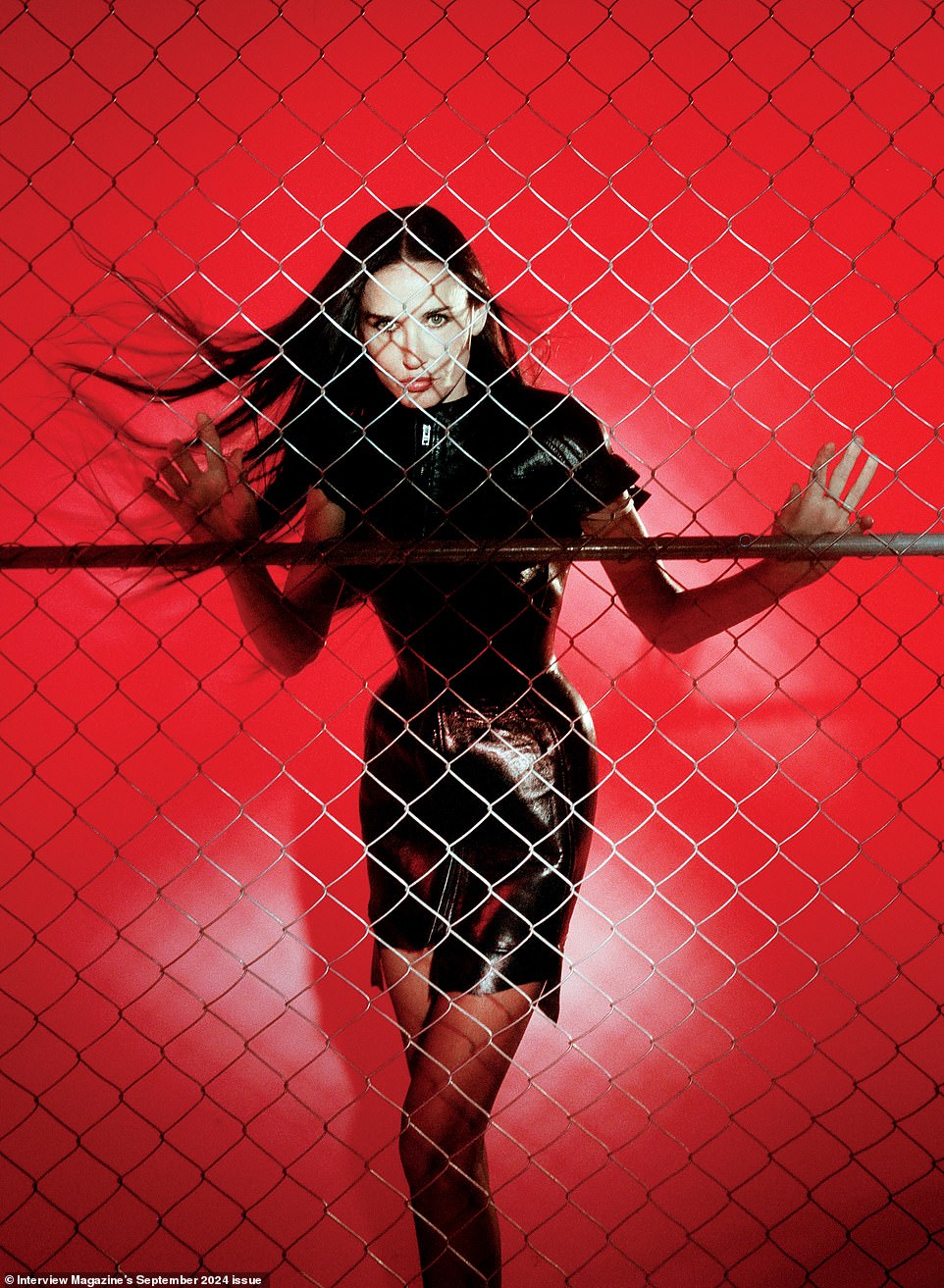 Moore wore a black leather dress as she posed against a red backdrop behind a fence