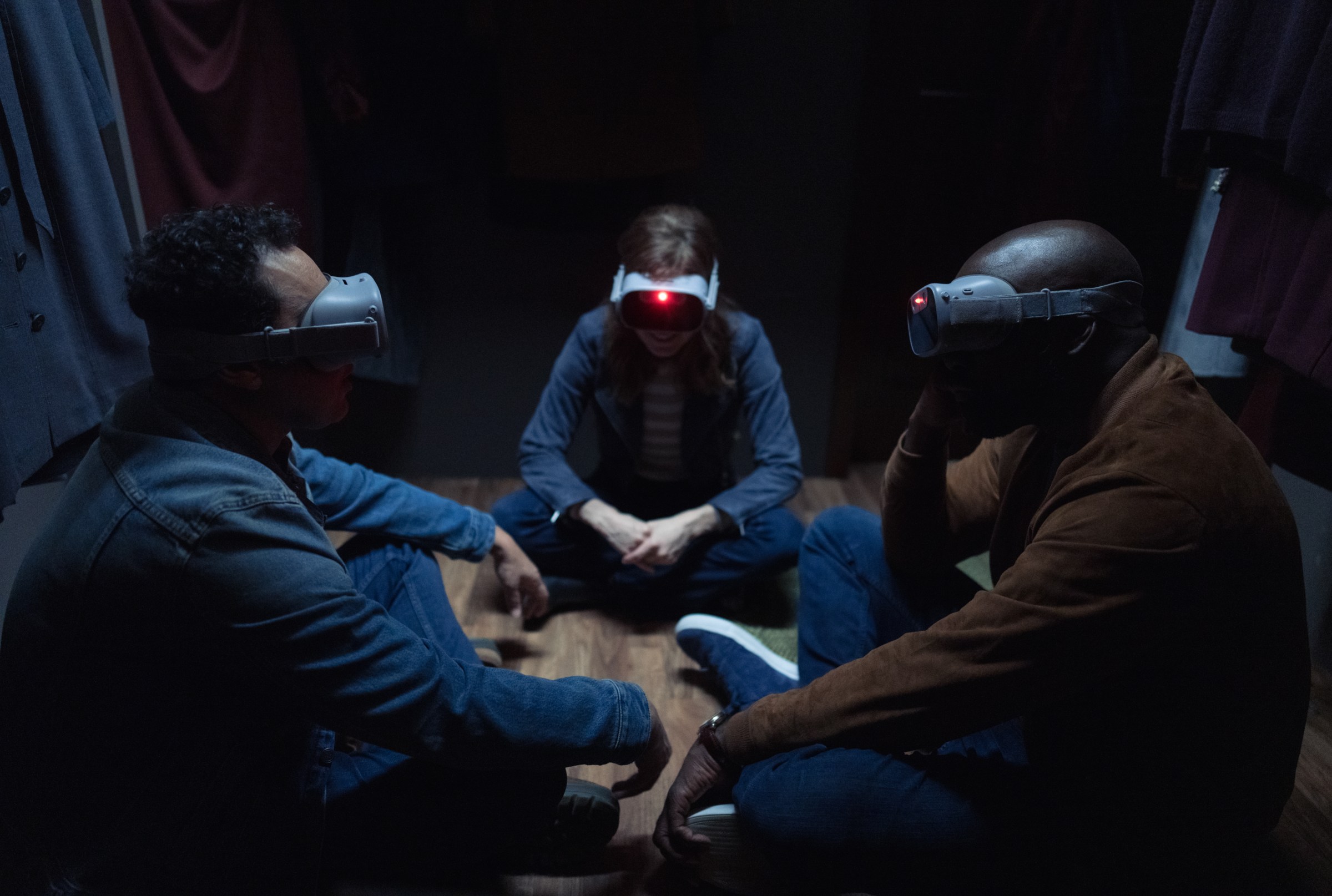 Ben, Kristen and David sit around with VR masks in a still from Evil