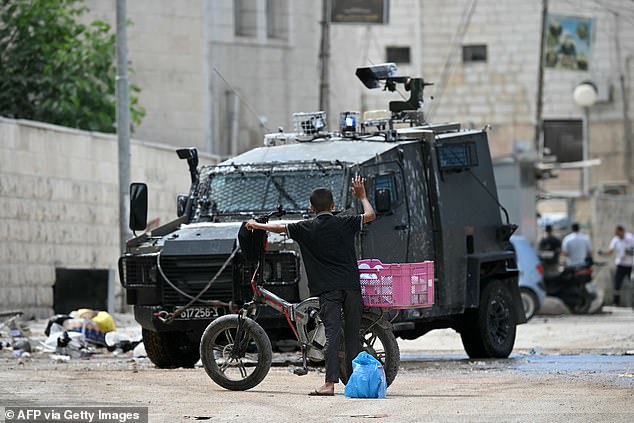 A Palestinian boy raises his arm in the air as Israeli soldiers inspect what he is wearing during a raid in Jenin