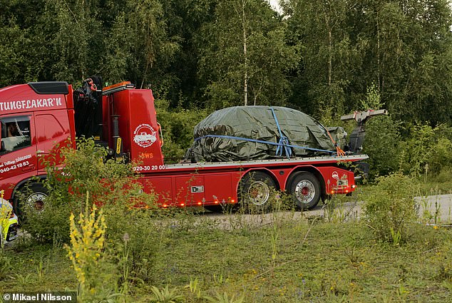 A truck is seen carrying the burnt-out car that was wrapped in a plastic sheet last month