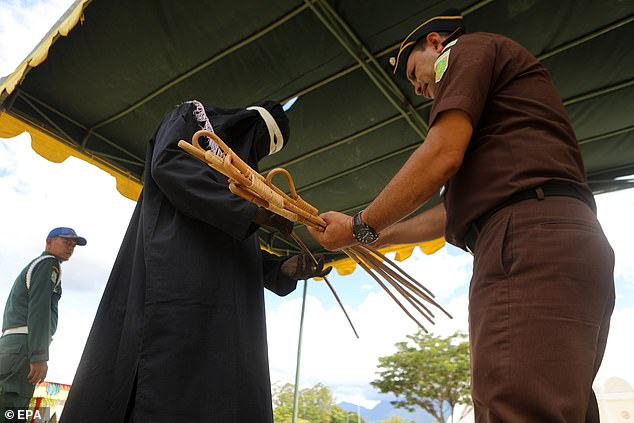 An officer holds a bundle of stiff wooden sticks, which he then hands to an algojo