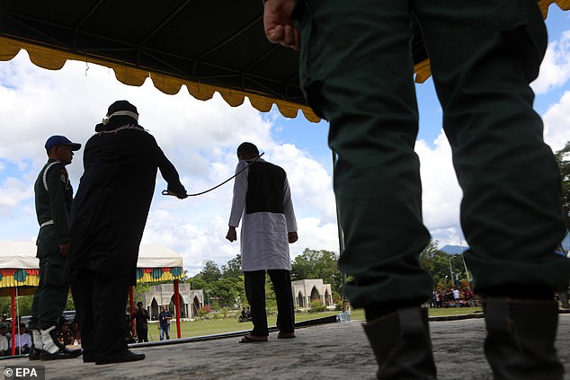 Officers watch as a man clenching his fists is beaten with a baton in Indonesia