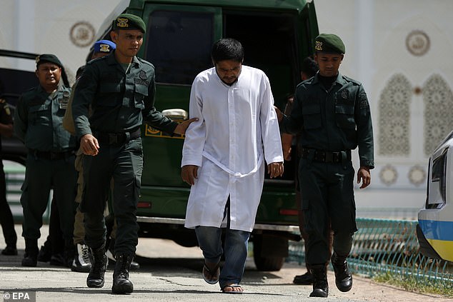 A man about to be publicly caned for violating Sharia law is escorted by Sharia police in Jantho