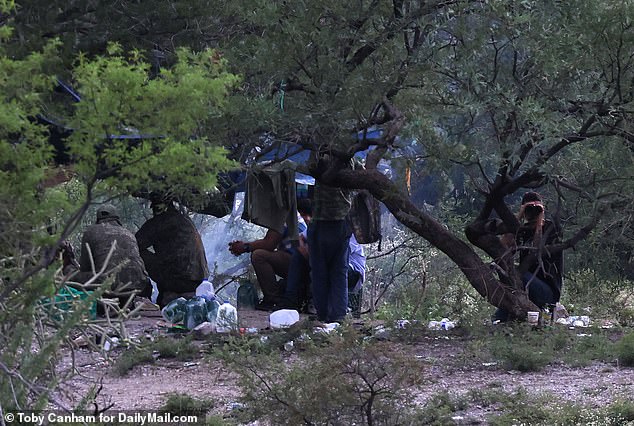 Migrants set up camp in Mexico, just yards from the U.S. border wall, as they prepare to cross. One of them looks out with binoculars.