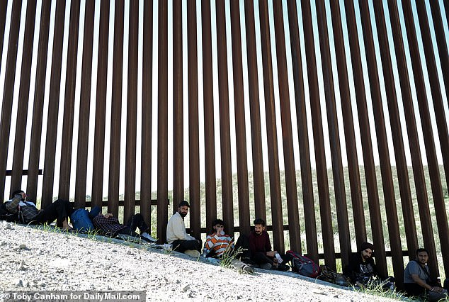 A group of migrants from India wait in the shadow of the border wall for a ride from the border patrol