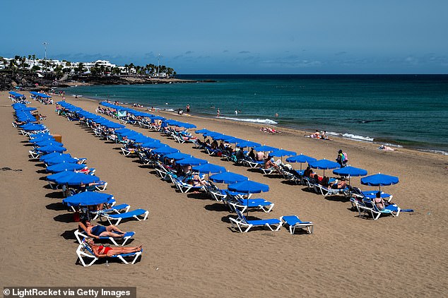 Tourists sunbathe, swim and relax on Playa Grande beach in Puerto del Carmen, located in the southeast of the volcanic island of Lanzarote