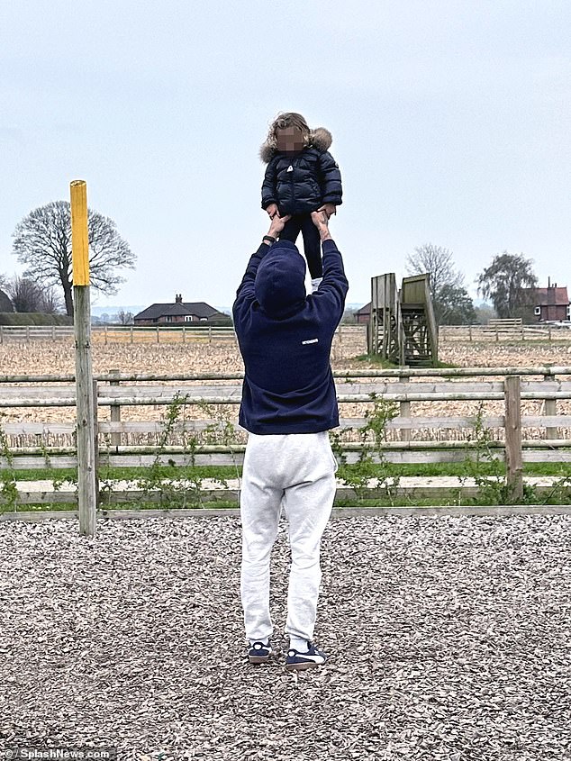 Dressed in a navy jacket and baseball cap, the 34-year-old is pictured throwing his son into the air