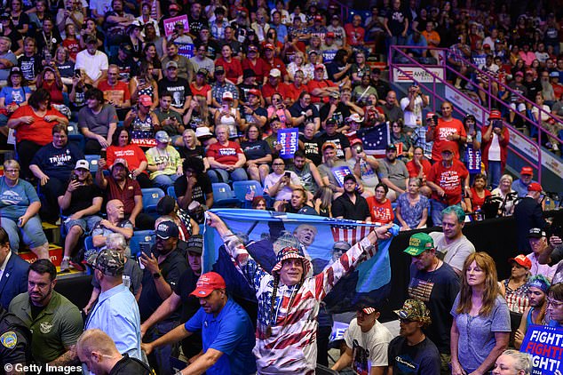 A man holds a flag as another man is arrested by security and police after jumping onto the media platform during a campaign rally for the Republican presidential candidate