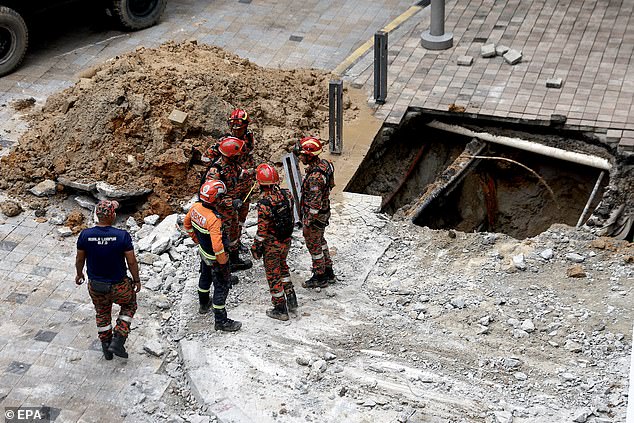 Malaysian Fire and Rescue Service officers inspect the scene where a woman fell into an eight-metre deep sinkhole