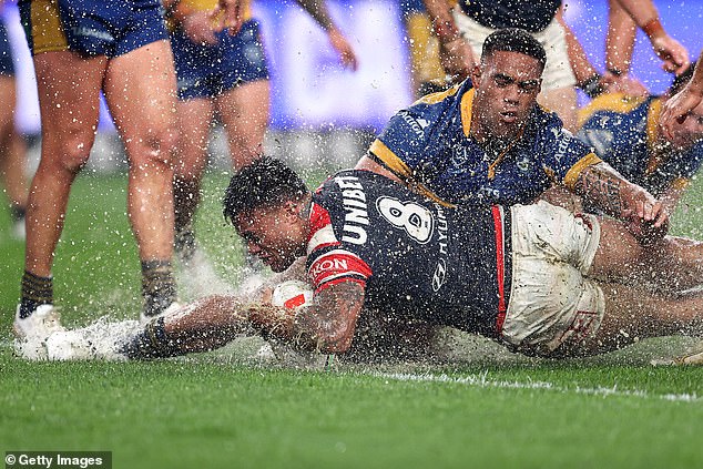 Roosters' Spencer Leniu scores a try by sliding through a huge puddle of water at Allianz