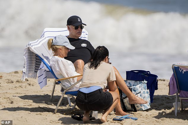 Joe Biden sat next to a blue umbrella wearing a black hat and a Philadelphia Eagles T-shirt while talking on the phone