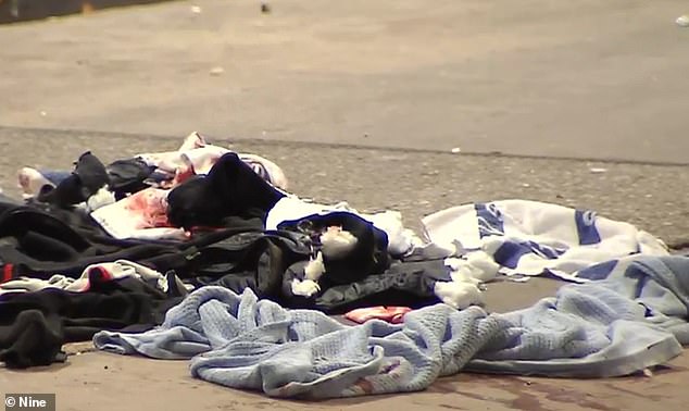 A boy, reportedly aged 17, was stabbed by a group of about 10 knife-wielding assailants in the car park of a shopping centre in Melbourne's west (pictured: blood-stained clothing at the crime scene)