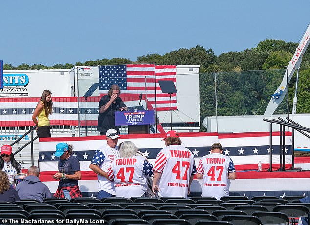 The stage and seating are carefully placed between hangar buildings and stacks of shipping containers, to shield the rally site