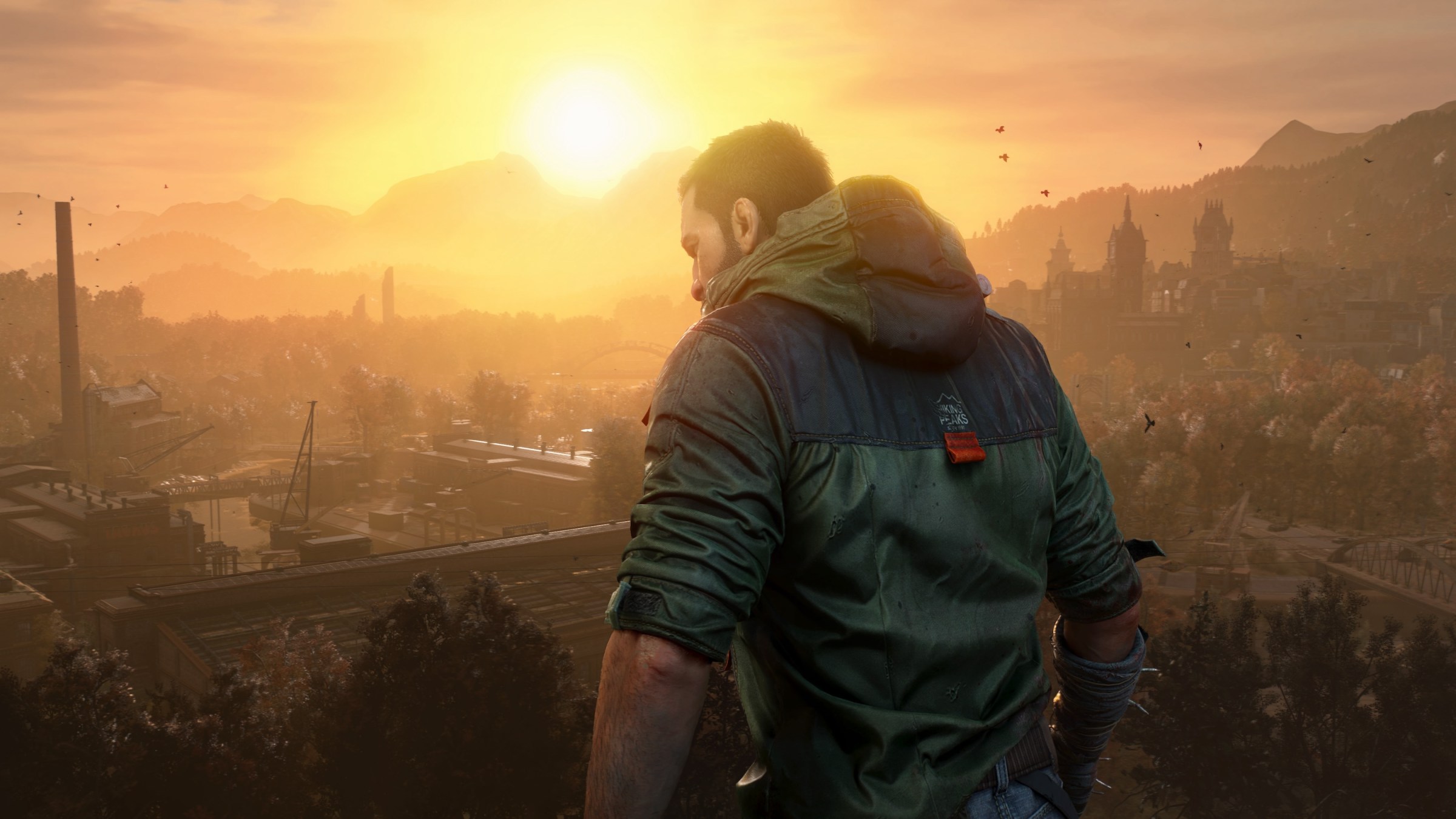 A screenshot from Dying Light: The Beast shows main character Kyle Crane standing in front of a sunset with a video of a city in the background.