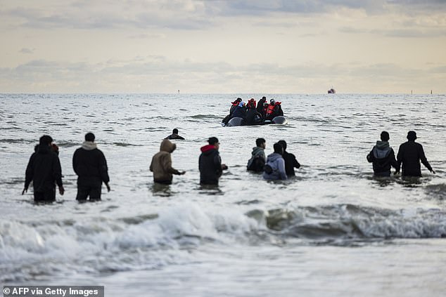 File photo. Migrants walk through water to board a smuggling boat on the northern coast of France