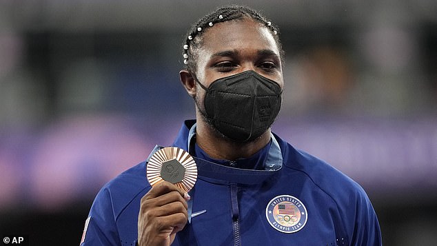 A masked Noah Lyles stands on the podium after winning bronze in the 200-meter final