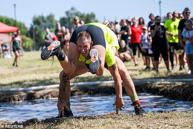 A group of men today scrambled through rough terrain and muddy puddles, dragging their partners on their backs, in an attempt to be the first to cross the finish line