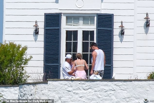 Travis Kelce (R) and Taylor Swift (C) sit with Patrick Mahomes on the balcony of the mansion