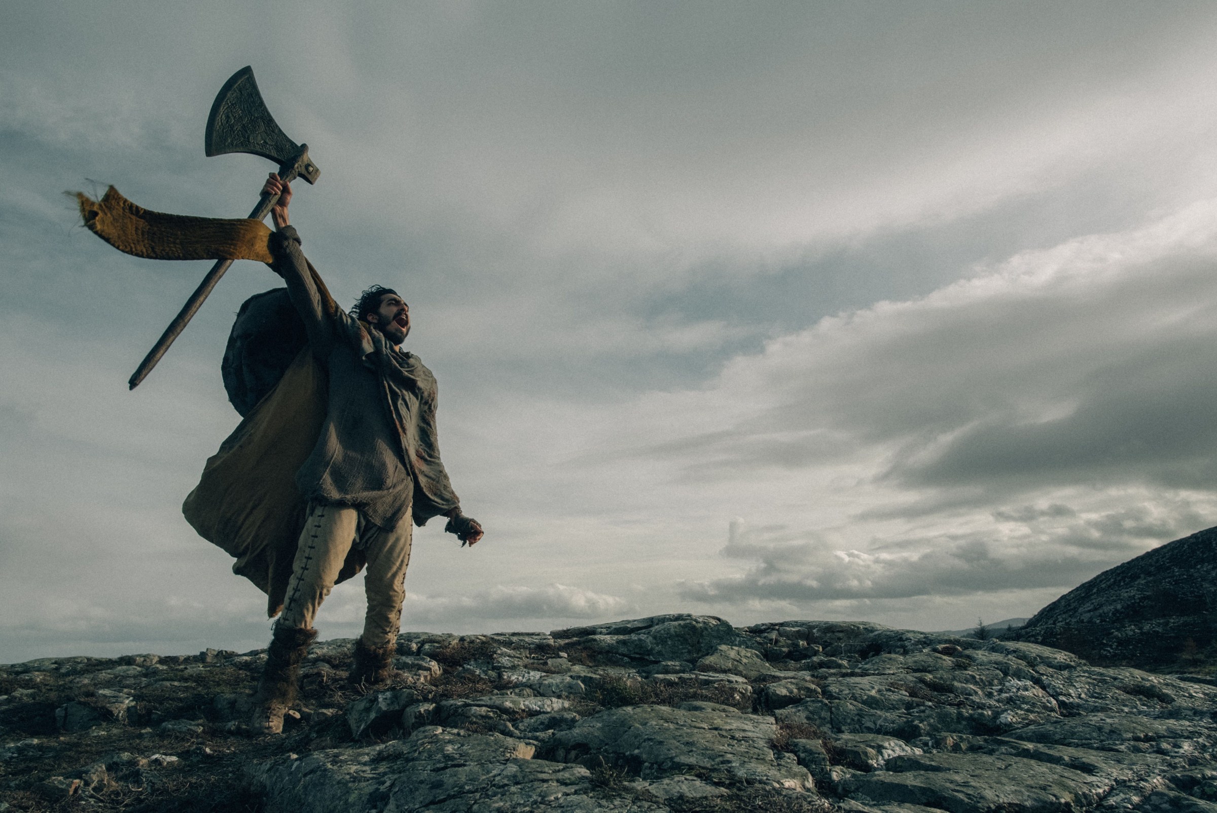 Dev Patel as Sir Gawain lifting an axe and screaming on top of a mountain in The Green Knight