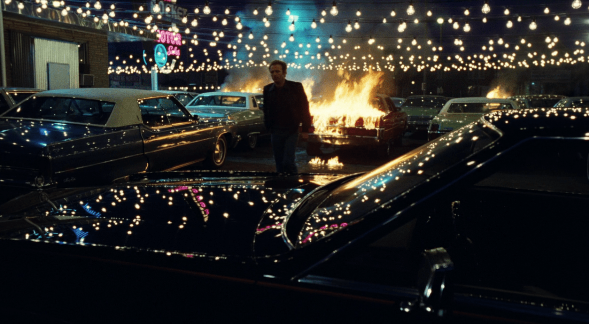 James Caan in Thief stands under several lights with a burning car behind him