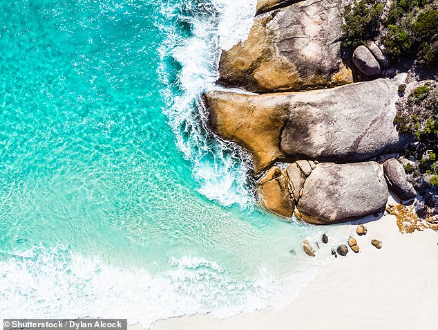 Iconic giant boulders lie scattered across pristine white sand next to water so blue it's 'unbelievable' - visitors to the beach find the rocks harder to climb than they look