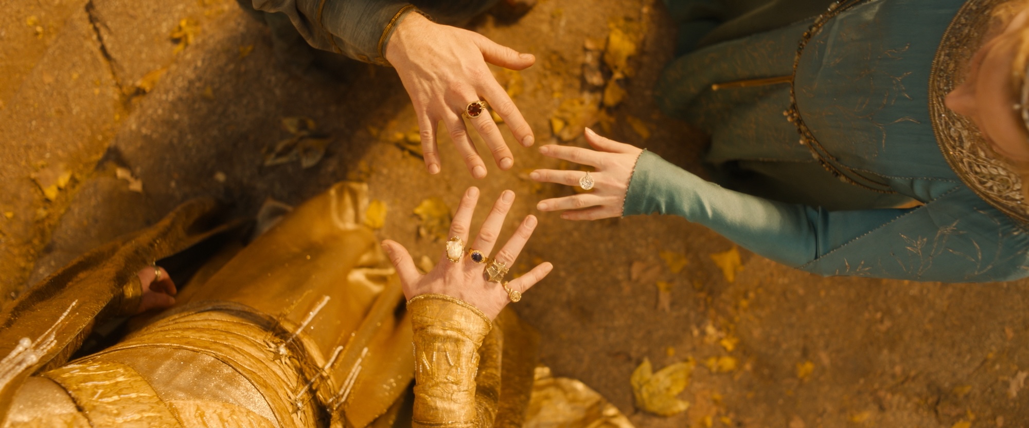 The hands of Galadriel, Gil-galad, and another elf, wearing the three elf rings in The Lord of the Rings: The Rings of Power. 