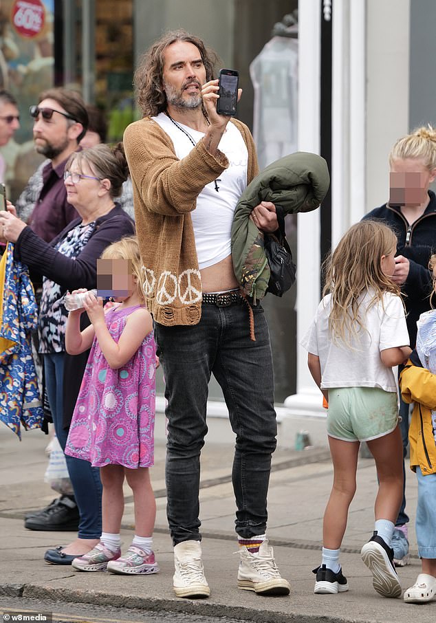 Russell looked casual in a brown cardigan with a white peace symbol T-shirt and black skinny jeans as he filmed the event on his mobile phone while mingling with other tourists