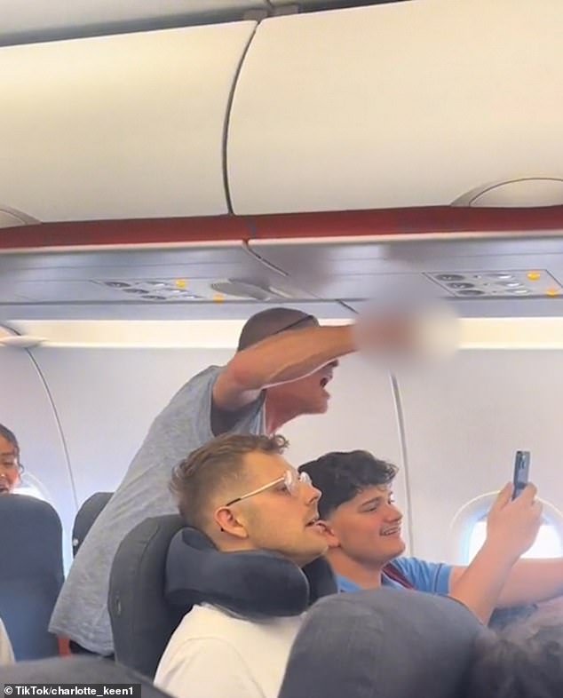 Passengers were furious after the drunk passenger caused their flight to be diverted to Munich after he tried to open the emergency exit during the flight (pictured: an angry passenger telling the unruly flyer to 'get out')