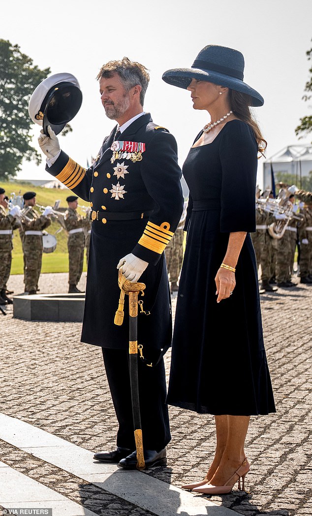 King Frederik is photographed removing his hat as he takes part in the wreath-laying ceremony with Mary