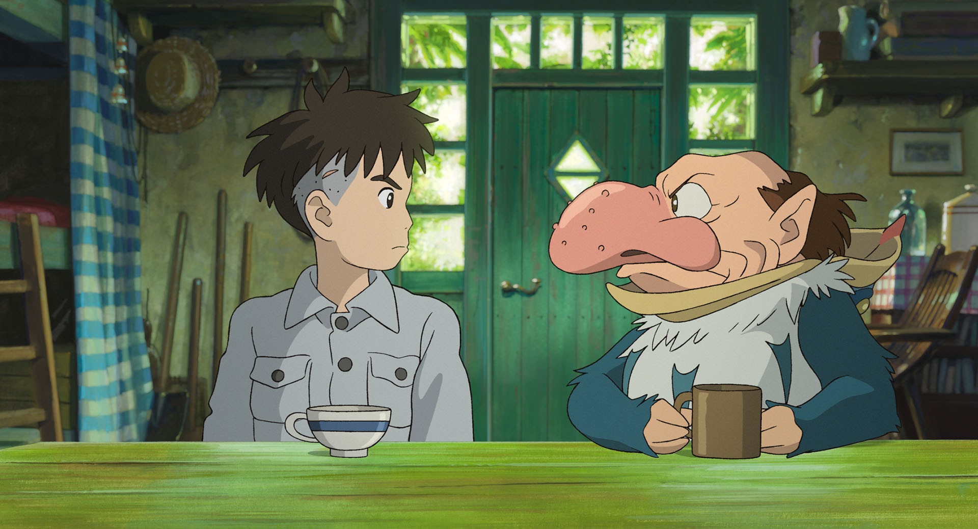 A stubborn-looking boy with shaggy hair and an undercut sits at a table opposite a small man with a huge, pimple-covered nose and a bald head with brown bangs around his pointy ears, dressed in a blue-and-white feather suit and holding a brown mug, in Hayao Miyazaki's The Boy and the Heron