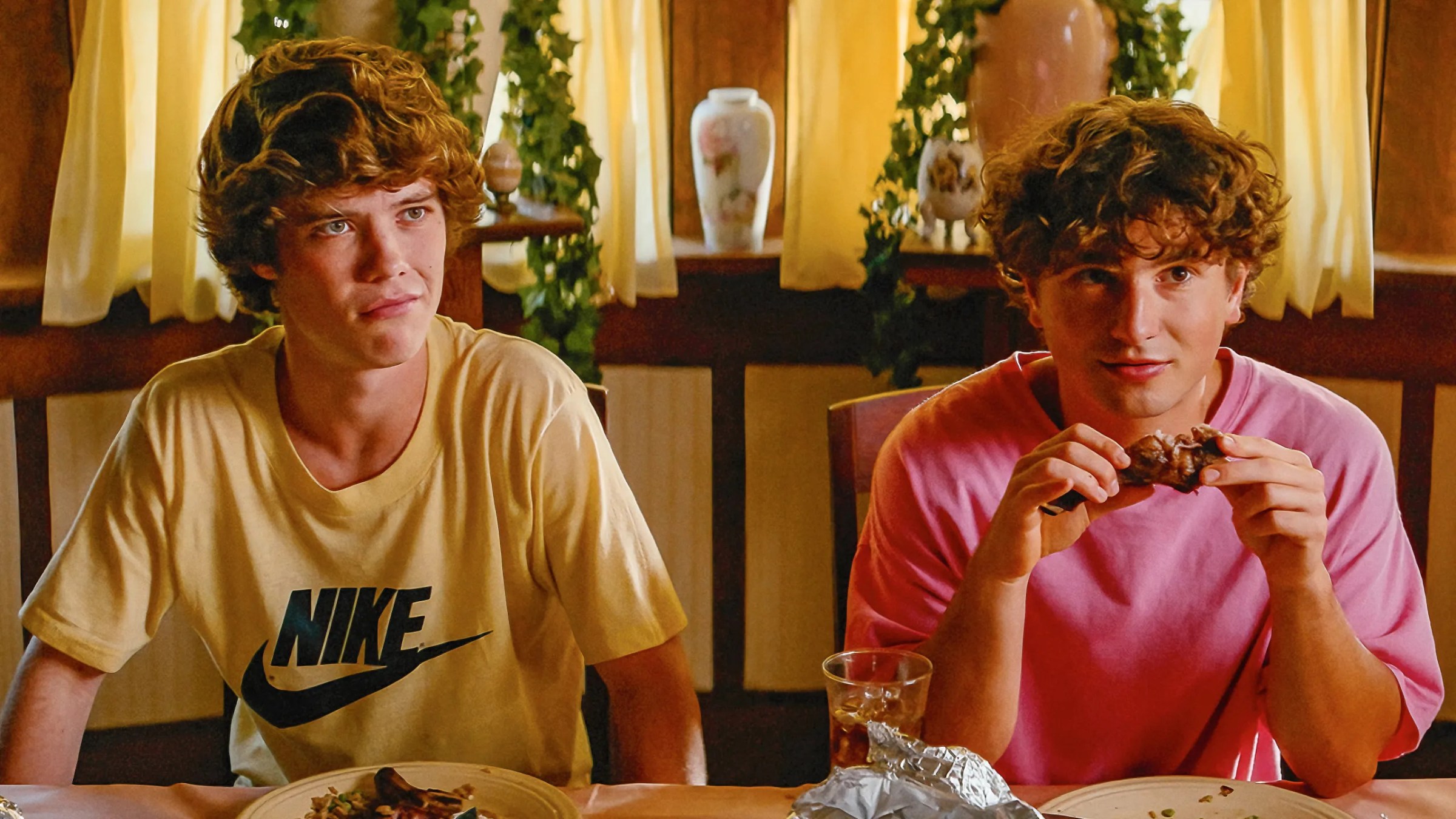 A man in a yellow Nike shirt and a man in a pink shirt hold a piece of chicken in Snack Shack.