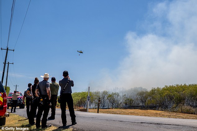 Members of the Hays County Emergency Service Districts and the Kyle and Buda Fire Departments watch as a helicopter prepares to drop water on a wildfire during an extreme heat warning in August 2023