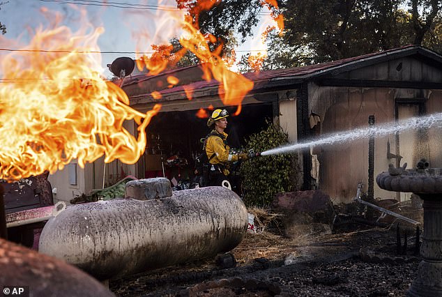 Firefighter Nolan Graham sprays water around a charred garage as the Boyles Fire rages in Clearlake, California, on Sunday, September 8.