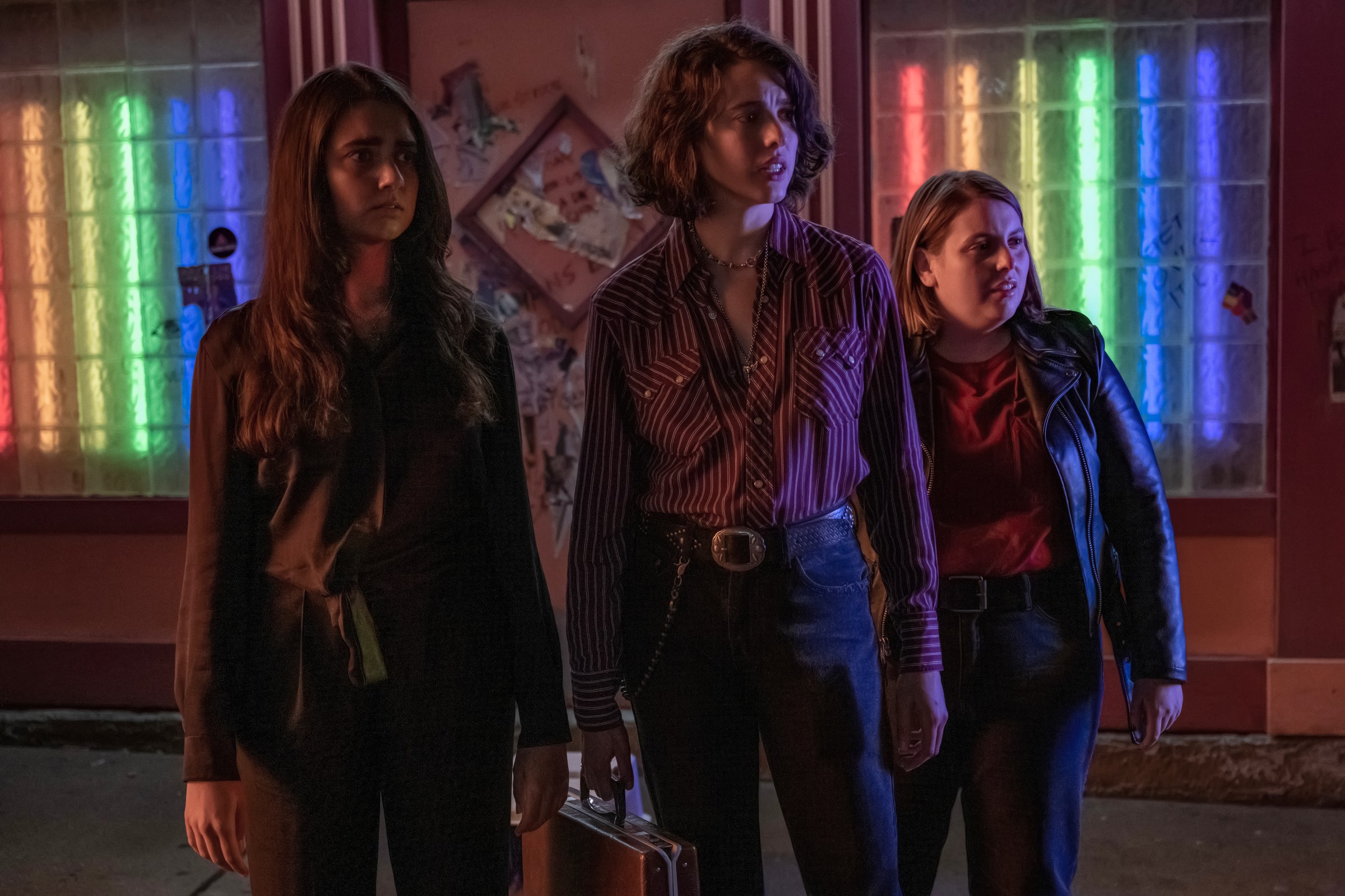 Geraldine Viswanathan, Margaret Qualley and Beanie Feldstein stand outside what appears to be a bar in Drive-Away Dolls