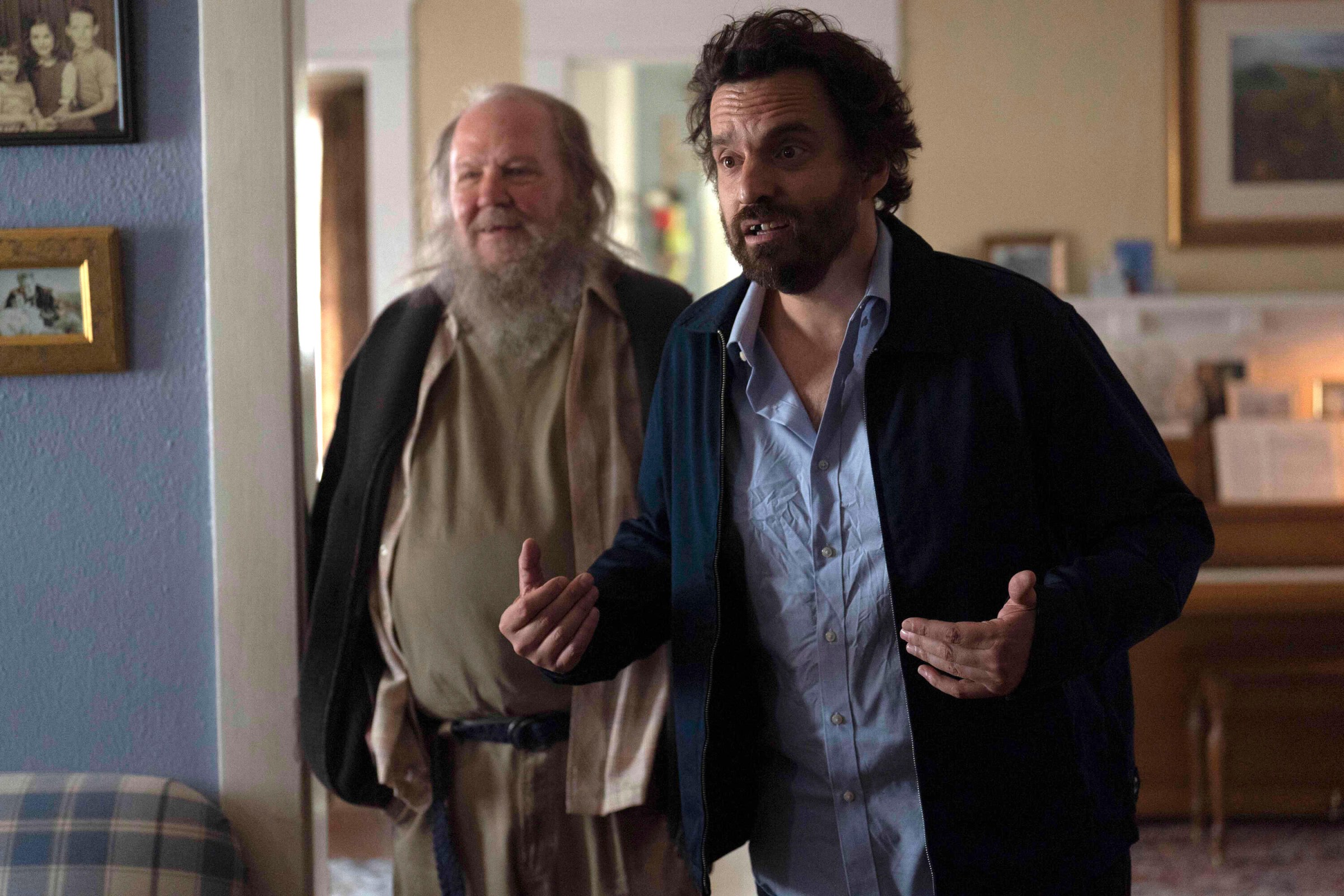 Tommy (Jake Johnson) and a friend (Biff Wiff) stand together in a living room as Tommy earnestly tells a story to someone off-screen in Self Reliance