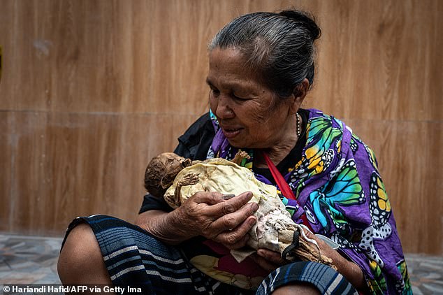 A member of the Toraja ethnic group holds the exhumed body of her baby who died in 1988, during the traditional ritual known as Manene in Pangala, South Sulawesi, on August 27, 2024