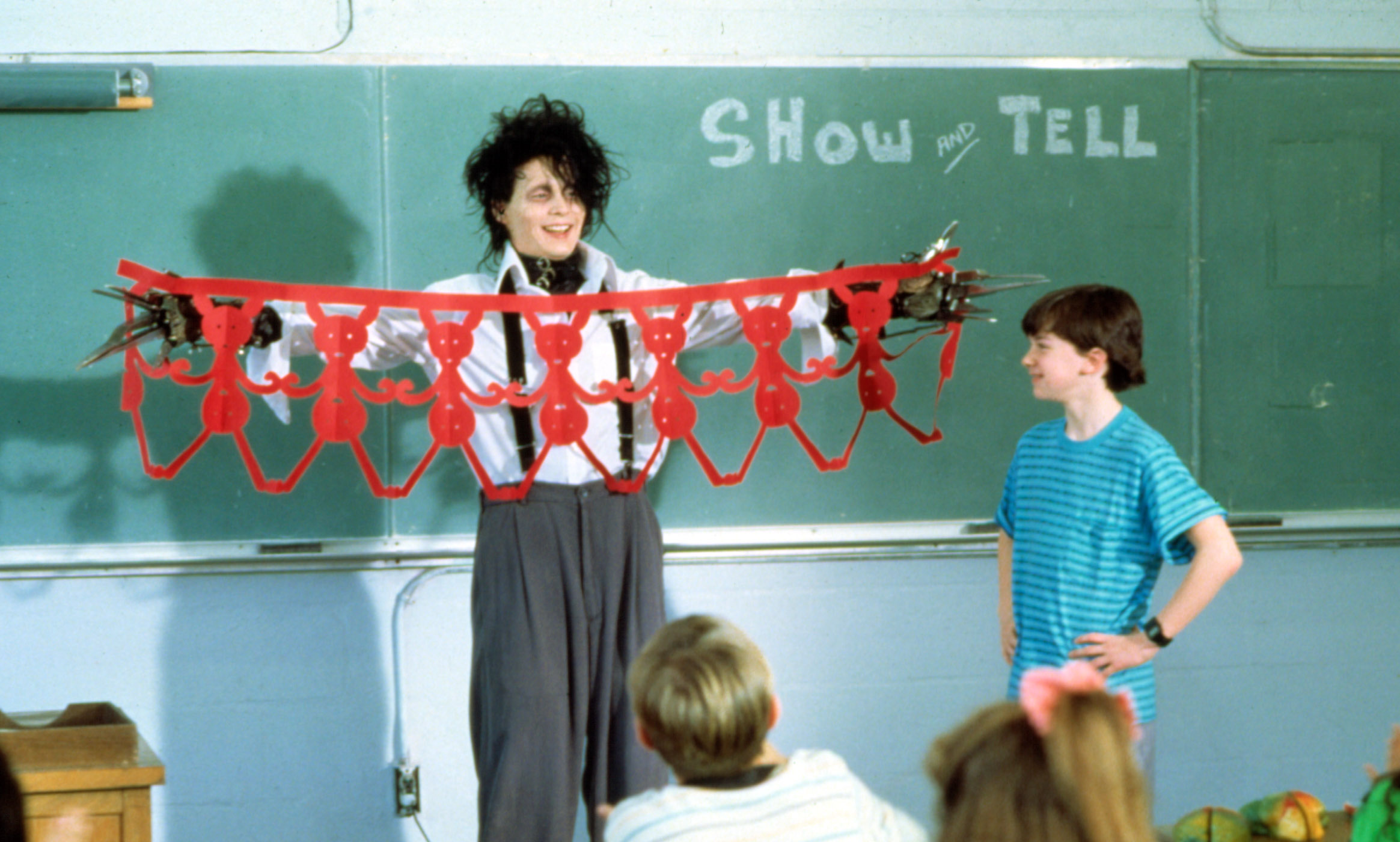 Edward Scissorhands (Johnny Depp) laughs as he shows a row of red paper dolls to an elementary school class in Edward Scissorhands