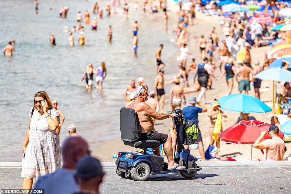 A man riding a mobility scooter is seen riding along the beach in Benidorm