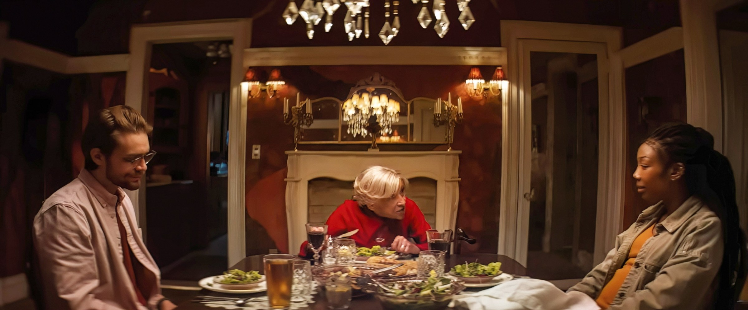 Norman (Andrew Burnap) and Belinda (Brandy Norwood), a mixed-race middle-class couple, sit on either side of a dining table next to Norman's elderly mother Solange (Kathryn Hunter) in Sam and Max Eggers' horror film The Front Room.