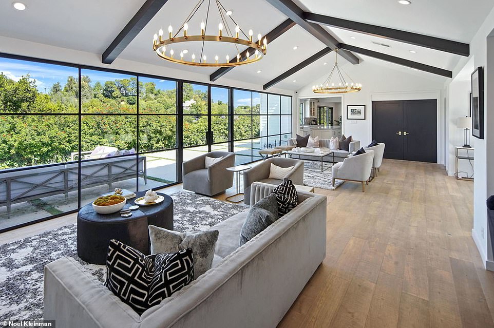 The interior features an angular, minimalist design with off-white walls with black ceiling beams and hardwood floors