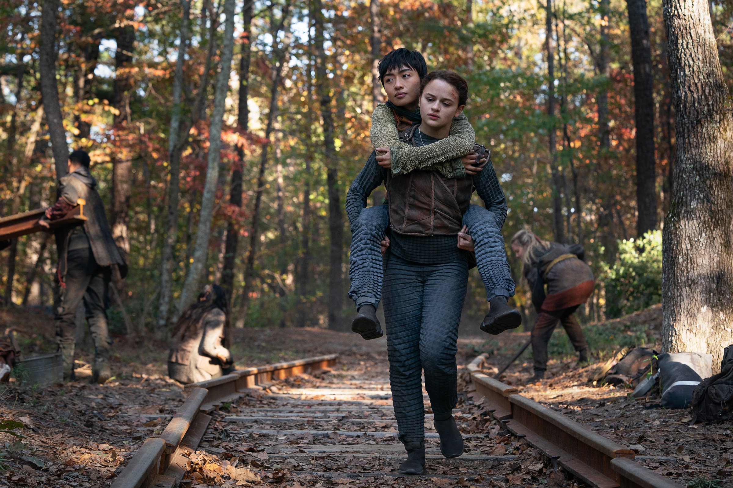 Tally (Joey King) carries Shay (Brianne Tju) on his back as they trek through a forest in the Netflix series Uglies.