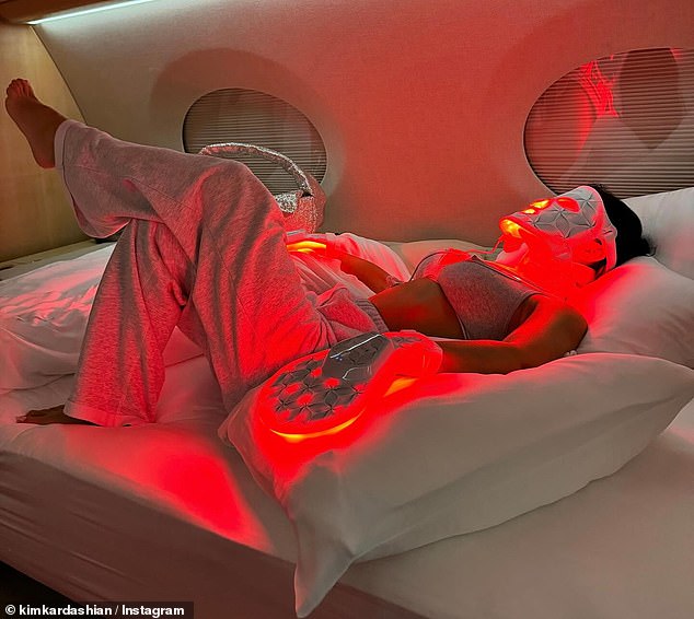 The SKIMS founder gave viewers a glimpse into her extravagant lifestyle with a photo of herself receiving a red light therapy mask treatment while lying in bed wearing only a bra and sweatsuit while sitting in her jet