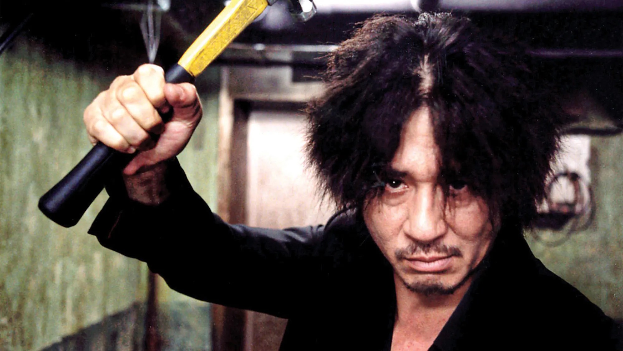 Oh Dae-su (Choi Min-sik), a man with wild hair holding a hammer menacingly above his head, looks into the camera in Oldboy