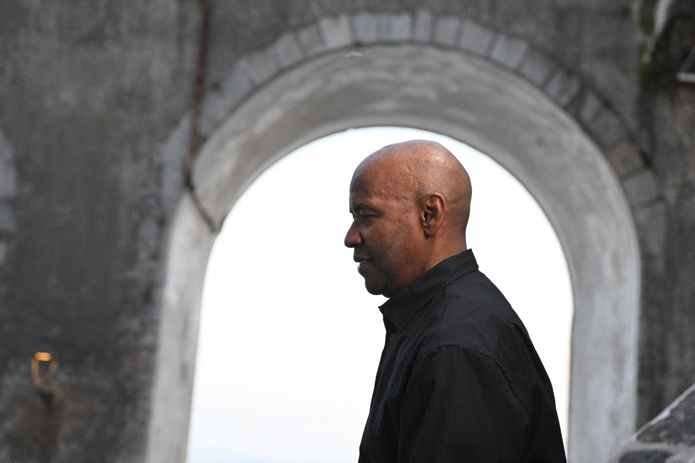 Denzel Washington wears all black on the Amalfi Coast and is surrounded by a stone building on the set of Equalizer 3.